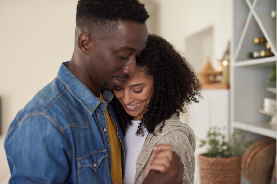 Loving young multiracial couple smiling and dancing in their kitchen