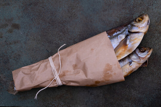 Two dried fish wrapped in a brown parchment paper bag lay on a rustic surface, showcasing traditional packaging of seafood.