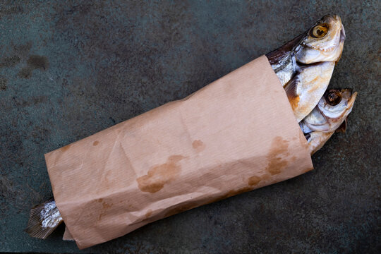 Two dried fish wrapped in a brown parchment paper bag lay on a rustic surface, showcasing traditional packaging of seafood.