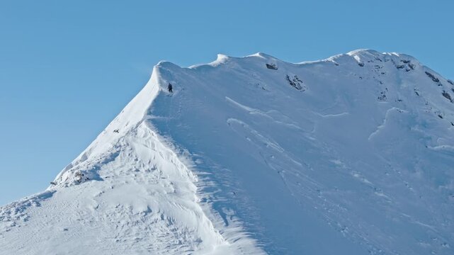 Slow motion aerial footage of a free ride skier carving through fresh powder snow on a steep alpine slope. Dynamic drone shot capturing the thrill of first tracks in pristine winter mountains.
