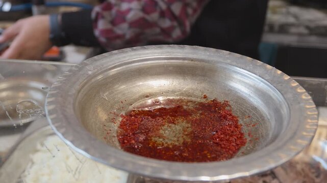Chef preparing traditional Turkish Beyran soup by mixing red chili flakes with hot broth.