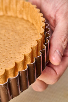 Baked shortcrust tart shell in metal ring held by hand. Pastry preparation process, bakery base for desserts and tarts.
