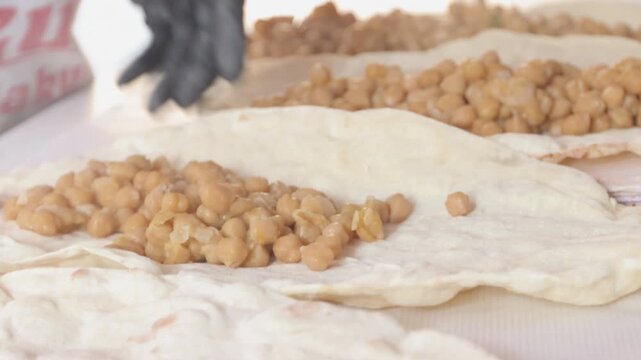 Chef hands preparing traditional Turkish chickpea wrap (Nohut Durum) on flatbread