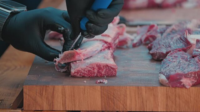 A butcher in black gloves carves fresh beef ribs on a wood cutting board. Close-up highlights the preparation of meat for grilling or a barbecue. Professional culinary concept