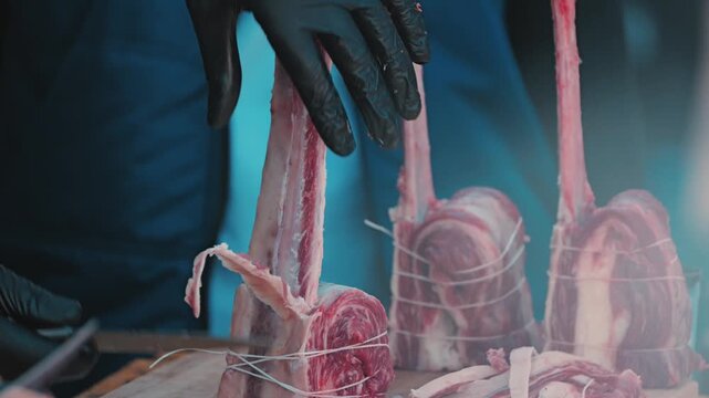 Close-up of a butcher's hands in black gloves expertly cutting raw tomahawk steaks. Professional food preparation on a wooden board, showcasing culinary skill with high-quality fresh meat
