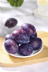 Fototapeta premium Fresh Purple Plums on Wooden Board - Sweet Healthy Fruit Snacking Style