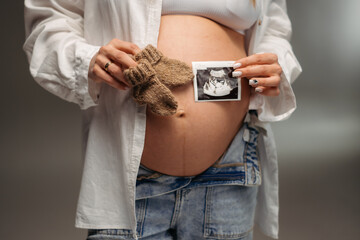 A pregnant woman holds an ultrasound image of her baby on her rounded belly. A tender and touching moment of anticipation