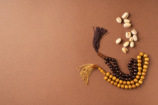 Ramadan kareem background with rosary, pistachios on brown background, copy space