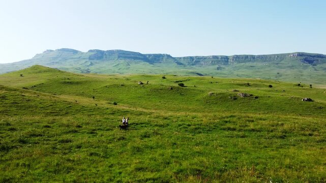Aerial video of girl and mother walking on field hills and playing with lovely dog in mountains on background. Drone flight to spectacular nature. Travel vacation in nature reserve, park