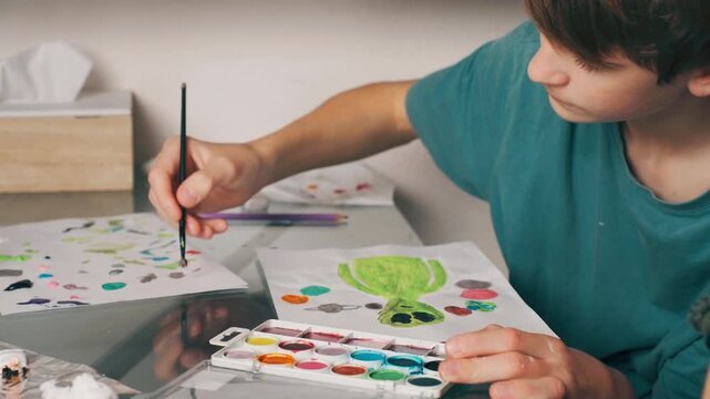Teen boy concentrating while painting picture at home. Focus, attention and creative thinking indoors, creating artwork at table during creative home activity