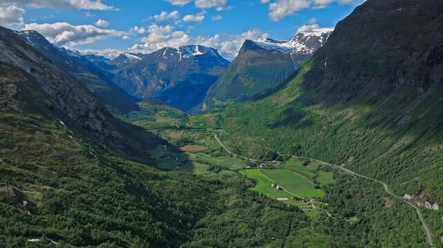 Aerial perspective sweeping over a long valley corridor with dense forests and cultivated land below. Sunlit slopes and layered mountains create strong depth and scale.