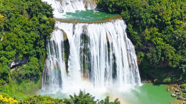 Aerial view of majestic Huangguoshu Waterfall cascading into a blue river surrounded by lush green forests in Guizhou, China.