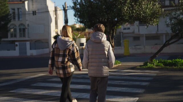 Back view of mother and teenager son  strolling together across zebra crossing on a sunny day. Family  enjoy walk through city, dressed in warm, casual winter jackets