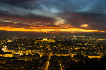 Fototapeta premium Panorama of Athens at sunset with a view of the Acropolis. The city lit up at night against the backdrop of enchanting clouds and a mesmerizing sunset. A peaceful picture of relaxation 