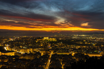 Fototapeta premium Panorama of Athens at sunset with a view of the Acropolis. The city lit up at night against the backdrop of enchanting clouds and a mesmerizing sunset. A peaceful picture of relaxation 