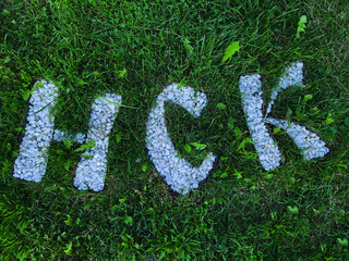 The letters are made of white stones on a background of green grass. The letters of the alphabet are made of stones in an original shape