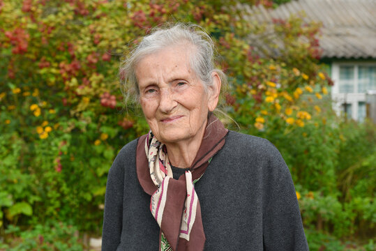 Portrait of a charming 89 year old woman, a rural resident, smiling in an autumn garden, near a village house.