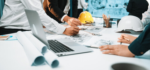 A diverse group of professionals engaged in collaborative planning over construction documents in a modern office setting. Tools and technology enhance productivity. SACTR © InfiniteFlow