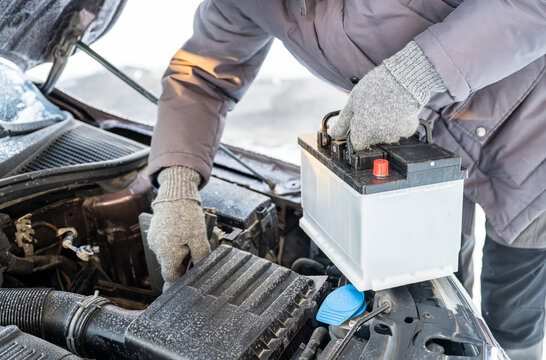 Man replacing car battery in winter cold with open hood during roadside emergency repair, emergency vehicle maintenance concept