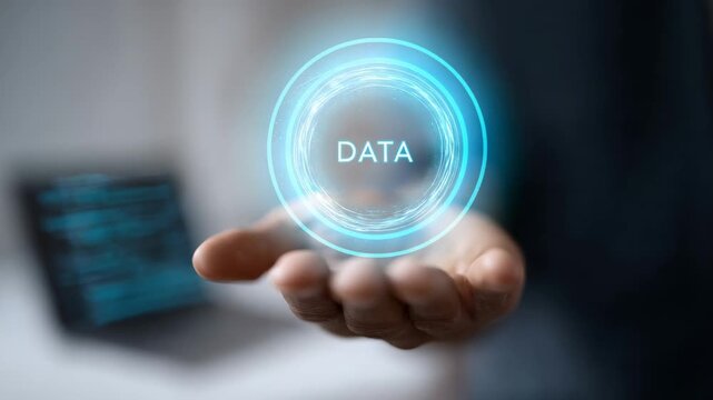 Businessman in dark suit presents glowing futuristic data symbol floating above open hand, with blurred computer screen displaying code in the background