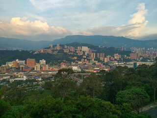 Obraz premium A city view set against mountains, featuring a mix of high-rise buildings, commercial blocks and lush greenery on rolling hills. Ideal for urban life, travel and landscape themes.