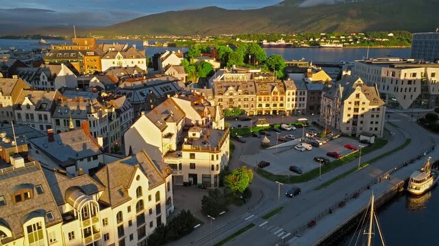 Aerial drone view of Alesund, Norway looking across a central square and surrounding streets at golden hour sunset.The norwegian view shows intersecting roads, mixed-height buildings, parked cars.