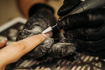 Hardware manicure procedure: a technician wearing gloves treats the nail with a professional instrument