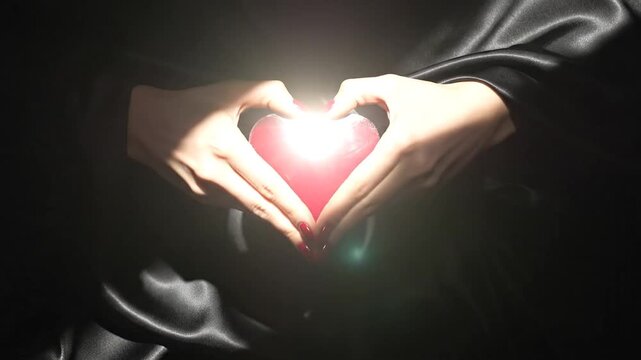 Manicured hands forming heart shape on black silk fabric texture Valentines Day