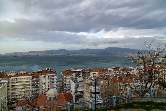 Panoramic view of the Karataş neighborhood and the Aegean Sea in Izmir, Turkey. Residential buildings with red roofs near the coast with mountains on a winter day in January.
