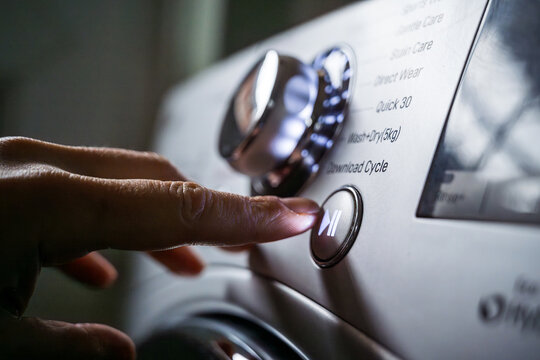 Washing machine, smart home appliances. Pressing start button on modern washing machine display. Daily chores, close-up shot