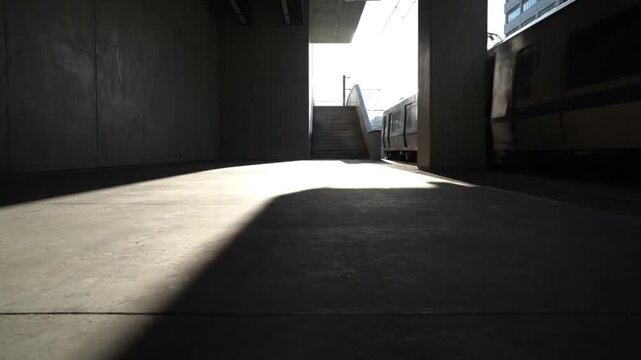 Bright sunshine illuminating empty concrete train station platform with a train passing through