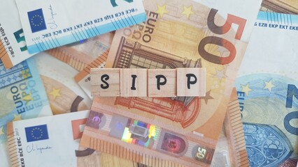 SIPP acronym made of wooden letter cubes on pile of Euro banknotes. Self-Invested Personal Pension