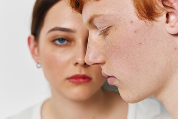 Fototapeta premium Closeup portrait of young man and woman with serious expressions on white background. Focus on natural skin details and emotional mood between two people.