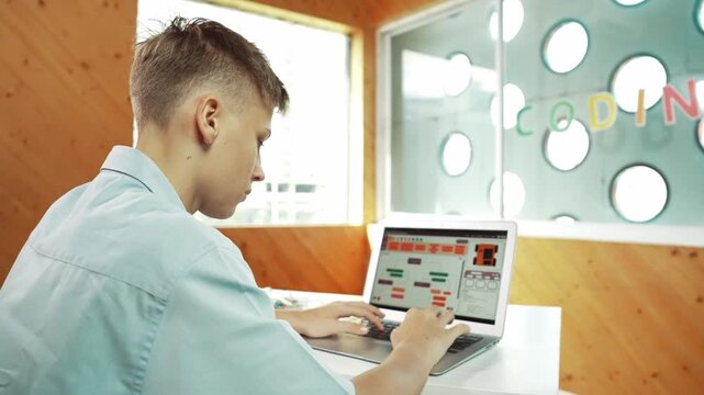 Back view of high school student working on laptop analysis data at STEM science class. Smart happy caucasian boy learning to coding engineering prompt or programming system at STEM class. Edification