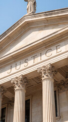 Naklejka premium The facade of a grand courthouse or government building features the word JUSTICE carved above classical columns, representing the legal system and rule of law