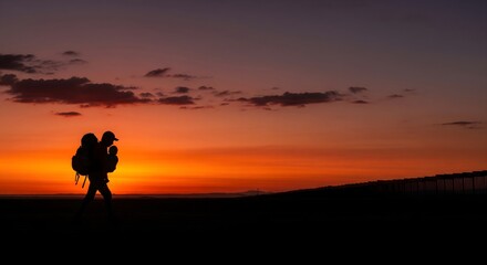 Obraz premium Solitary adventurer's silhouette walks towards a breathtaking orange and red sunset, marking the end of a day's inspiring journey
