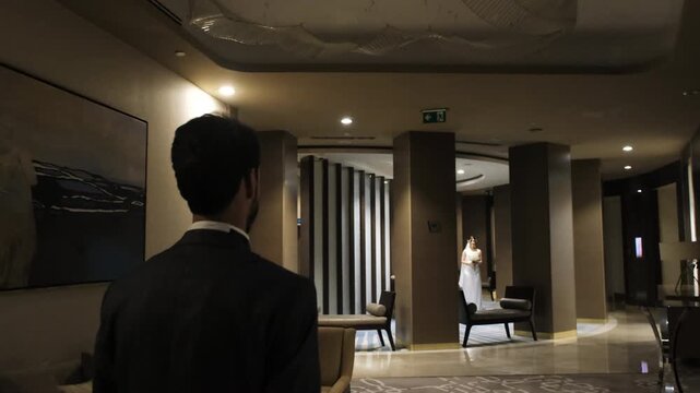 Groom in a suit walking through a luxury hotel lobby towards his bride for the first look