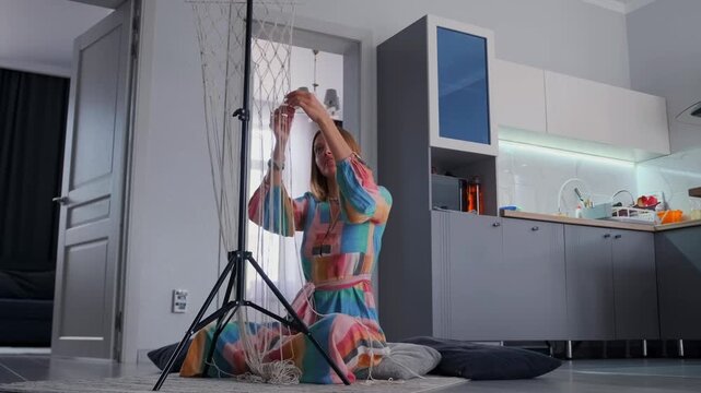 Happy woman weaving macrame threads at home -  creative handmade lifestyle with cozy atmosphere. Low angle.