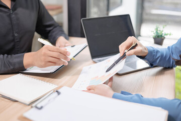 Obraz premium Two people are sitting at a desk with a laptop and a notebook. One of them is writing with a pen. The scene suggests a meeting or a discussion between the two people 