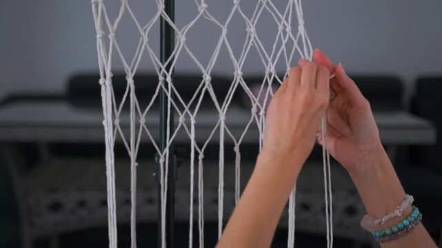 Young woman in colorful clothes tying knots and weaving macrame threads at home. Handmade craft -  cozy lifestyle and creative detail.