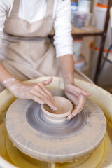 Fototapeta premium Close-up of hands shaping a clay bowl on a pottery wheel during a ceramics workshop. Creative craft process, handmade pottery, artisan skills and traditional craftsmanship.