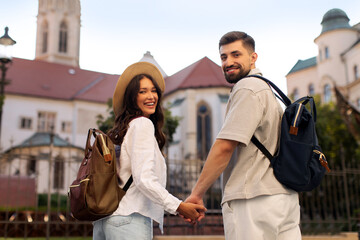 Fototapeta premium Happy European couple holding hands outside historic building while exploring the city together, turning back and smiling at camera