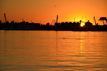 Naklejka premium Industrial port silhouette at dramatic orange sunset