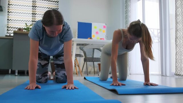 Two young women on yoga mats practicing cat cow pose indoors. Home workout for relaxation -  flexibility -  back health -  and fitness lifestyle.