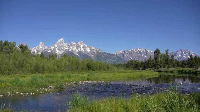 Wide shot of the Grand Teton Mountains with a river flowing through the valley in Grand Teton National Park, Wyoming. Expansive alpine landscape showcasing majestic peaks, serene water, and pristine n