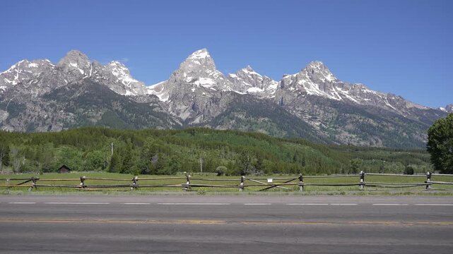 Grand Teton Mountains in the backdrop as a cyclist rides by and a car passes along a scenic road in Grand Teton National Park, Wyoming.