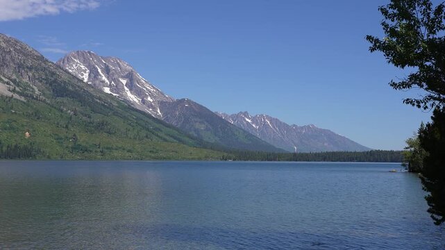 Slow zoom into the mountains in front of Jenny Lake in Grand Teton National Park, Wyoming. Cinematic alpine scenery featuring calm lake waters and the dramatic peaks of the Teton Range, highlighting d