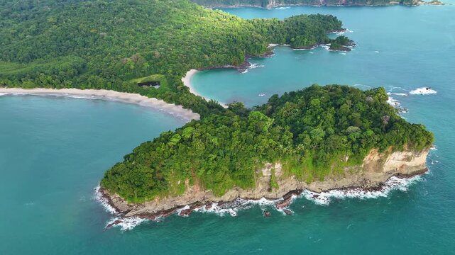High altitude orbit drone shot showing the full coastline and lush rainforest of Manuel Antonio National Park.