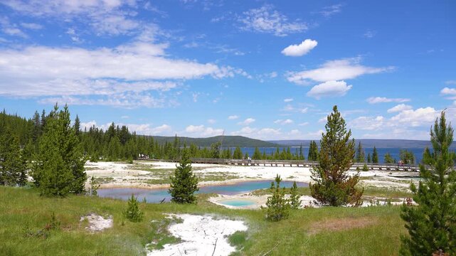 Super wide shot of a geyser with steam rising near a walkable path, Yellowstone Lake visible in the background at Yellowstone National Park, Wyoming.