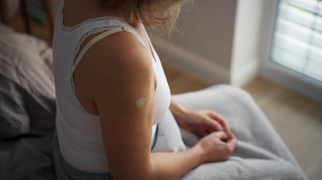 Woman applying estrogen patch during hormone therapy. Rear view.